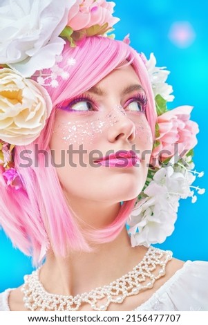 Spring and summer beauty. Portrait of a pretty teen girl with bright pink make-up posing in colored pink wig and flower wreath on head. Studio portrait on a blue background with lights. 