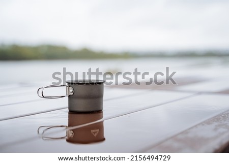 Aluminum mug stands on the table in a puddle of water, reflection in the water, tea glass, coffee mug hiking, travel to nature, camping food drink tea. High quality photo