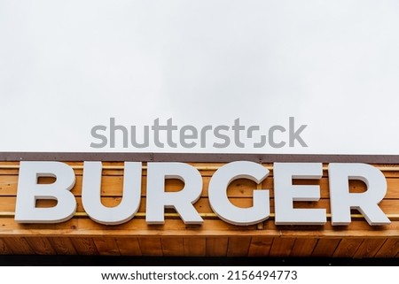 Burger restaurant logo, burger word sign in white letters, text written on a tree background, street restaurant, meat food, street food. High quality photo