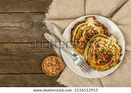 Homemade vegan cabbage steaks with herbs and spices. Healthy food ready to eat on a serving plate, cutlery. Old wooden background, top view Royalty-Free Stock Photo #2156512953