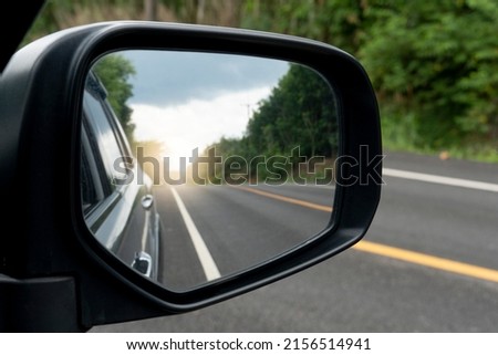 Inside view of mirrors wing. Rear view of a gray car with asphalt road and green trees in the daytime. Clear traffic in rural areas. Royalty-Free Stock Photo #2156514941