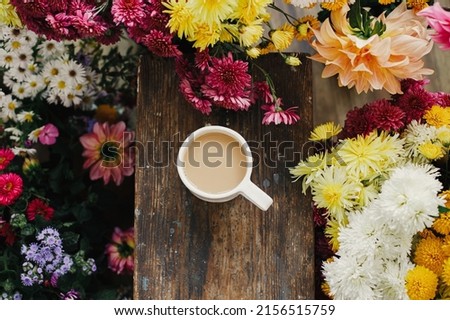 Warm cup of coffee and beautiful autumn flowers on rustic wooden background flat lay. Good morning. Stylish mug with cappuccino among colorful asters and dahlias composition. Moody image