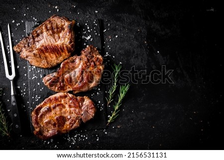 Grilled pork steak with a sprig of rosemary. On a black background. High quality photo Royalty-Free Stock Photo #2156531131