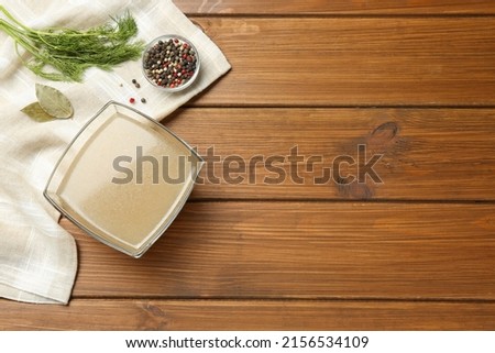 Glass bowl of delicious homemade bone broth, dill and spices on wooden table, flat lay. Space for text