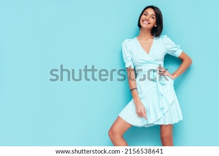 Portrait of young beautiful smiling female in trendy summer dress. Carefree woman posing near blue wall in studio. Positive model having fun indoors. Cheerful and happy. Isolated Royalty-Free Stock Photo #2156538641