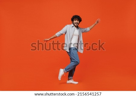 Full size body length side profile view jubilant young bearded Indian man 20s years old wears blue shirt dance waving fooling around have fun enjoy isolated on plain orange background studio portrait