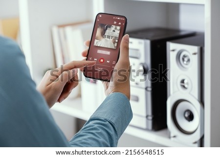 Woman playing music online on her stereo using her phone Royalty-Free Stock Photo #2156548515