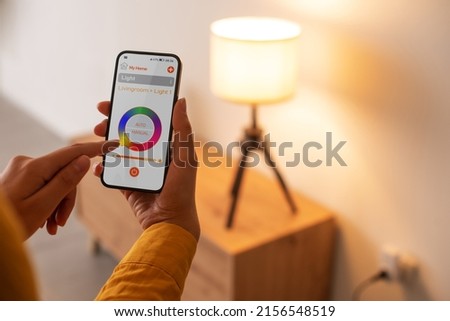 Woman controlling smart lighting at home, she is setting light color using her smartphone