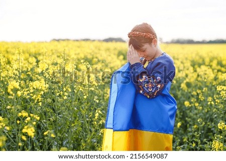 Pray for Ukraine. Child with Ukrainian flag in rapeseed field. Girl holding national flag praying for peace.