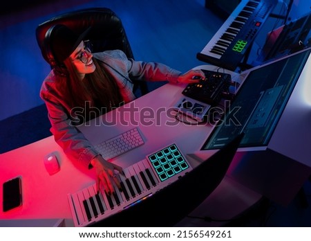 Beautiful caucasian girl in stylish clothes works in a recording studio with neon light in a cap and glasses Royalty-Free Stock Photo #2156549261