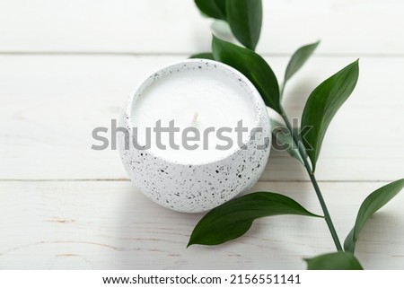 Composition with a candle and a sprig of a plant on a white table. Home interior. Space for text.