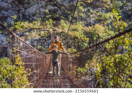 Father and son tourists on Old rusty bridge. Attraction Long extreme suspension iron bridge across the river Moraca. Sights of Montenegro. Landmark Montenegro Royalty-Free Stock Photo #2156559661