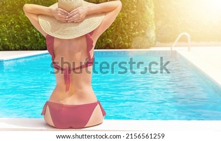 Girl siting near swimming pool and tanning, enjoying sunbeam. Female model in bathing suit, hat. Back view. Summer vacation, skincare, spa, wellness, cellulite treatment concept. Trogir, Croatia.