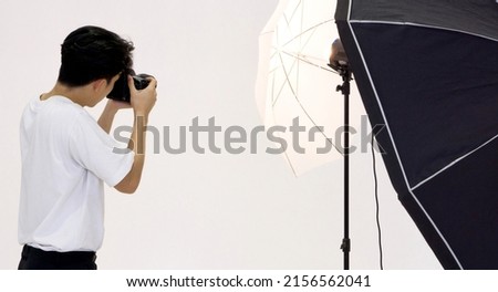 Asian photographer looks through the viewfinder while shooting with the camera. Working atmosphere in the photo studio.