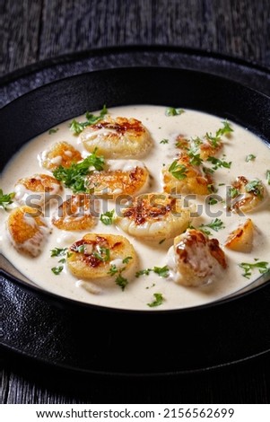 scallops in lemon, cream and white wine sauce in black bowl on dark wood table, vertical view from above, close-up Royalty-Free Stock Photo #2156562699