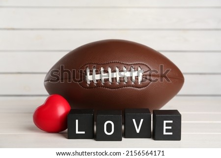 American football ball, heart and cubes with word Love on white wooden table