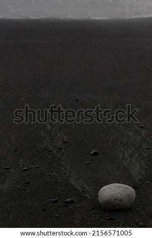 Wet black volcanic sand on shore with white stone, zen, texture, background, vertical.