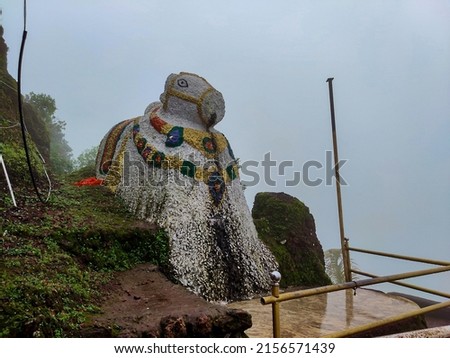 Stock photo of big ancient white color painted bull statue or Nandi at Sateri Mahadev Mandir, Nandi or bull is transport of lord shiva, Picture capture during rainy season at Kolhapur,India.