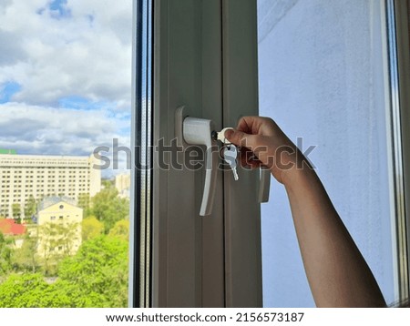 Small child opens window security lock with key. Child is in danger and the safety and protection of children. Royalty-Free Stock Photo #2156573187