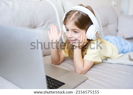 Smiling little girl wearing headphones using laptop, studying online, talking on video call, positive child schoolgirl, homeschooling concept