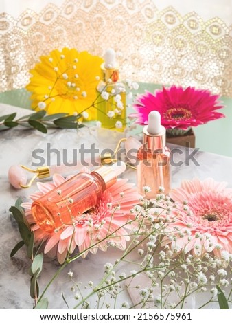 Beauty product face serum bottle and pink quartz face roller guasha on marble background with flowers. Natural skin care