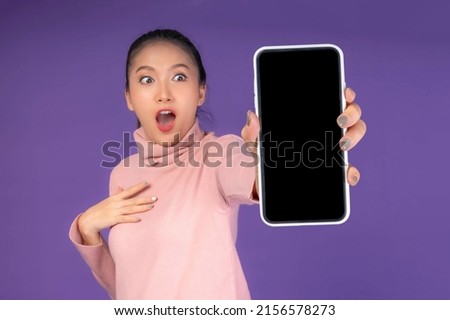 beautiful Asian young woman ,Excited surprised girl showing smart phone with blank screen , white screen isolated on purple background , Mock Up Image