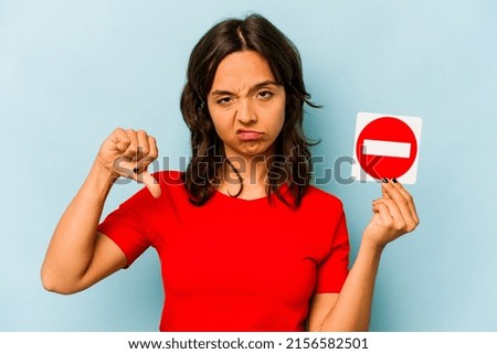 Young hispanic woman holding a forbidden sign isolated on blue background
