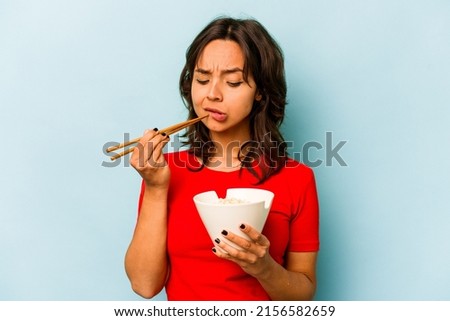 Young hispanic woman eating noodles isolated on blue background