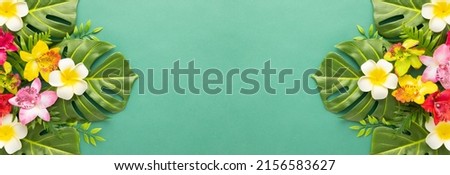 Summer background with tropical orchid flowers and green tropical palm leaves on green background. Flat lay, top view. Summer party backdrop.