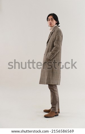 fashion model. side full body Young man with hairstyle in striped coat posing on gray background

