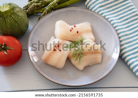 raw halibut fillet in a plate with fresh vegetables on a table