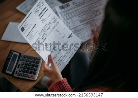 Close-up of female hands with pay slips, utility bills, account statements, payment receipts. A woman makes a count of household, family expenses with a calculator at home on the table. Royalty-Free Stock Photo #2156593147