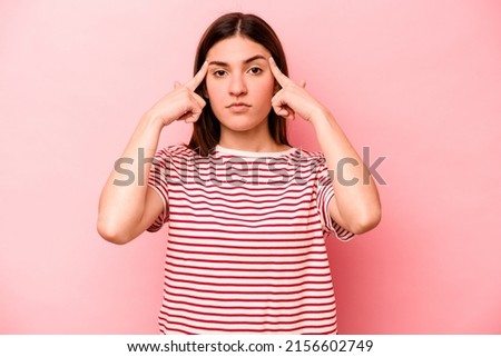 Young caucasian woman isolated on pink background focused on a task, keeping forefingers pointing head.