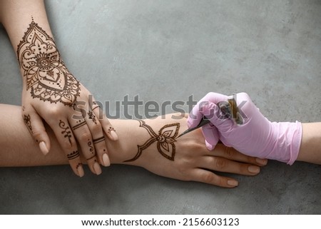 Mehndi master drawing henna tattoo on female hand in salon Royalty-Free Stock Photo #2156603123