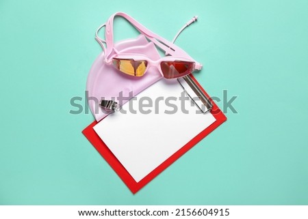Clipboard with swimming cap and goggles on blue background