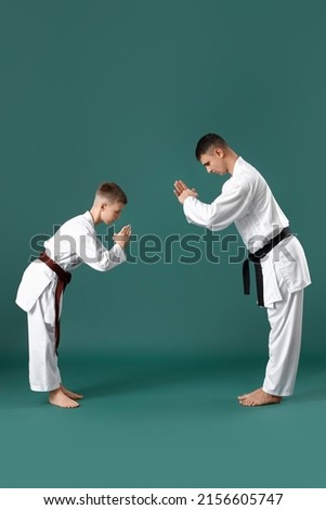 Boy and sensei performing ritual bow before practicing karate on green background Royalty-Free Stock Photo #2156605747