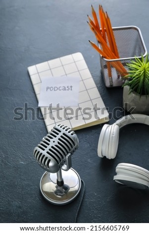 Microphone, headphones and paper with word PODCAST on dark background