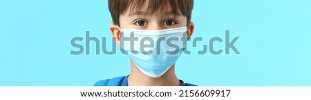 Little schoolboy in medical mask on light blue background