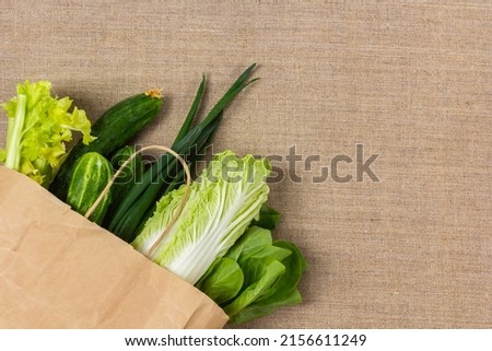 Fresh green vegetables in paper bag on burlap background and copy space. Delivery healthy food, grocery shopping, food supermarket and clean vegan eating concept.