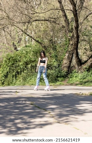 brunette woman in a sports bra, jeans and pink roller skates in a park