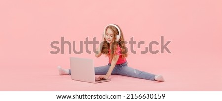 adorable child girl is sitting in the twine next to a laptop. kid in white headphones stretching and learns homework or watching cartoons, listening music.