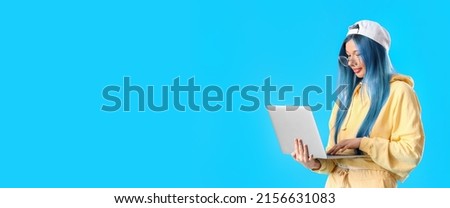 Cool young woman with long blue hair holding laptop on color background with space for text