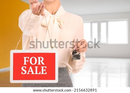 Female real estate agent with FOR SALE sign in empty flat