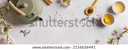 Green Tea and Cherry Blossom on white table, banner, copy space. Japanese cast iron teapot and cups, asian green tea composition with sakura bloom and petals. Royalty-Free Stock Photo #2156636441