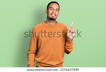 Young african american man wearing casual clothes with a big smile on face, pointing with hand finger to the side looking at the camera. 