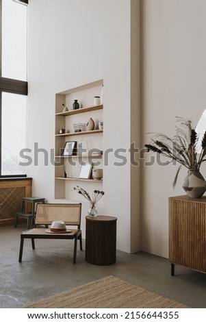 Aesthetic bright sunny elegant home living room interior design with comfortable lounge rattan chair, hat, side table, flowers bouquet, shelf with decorations. Scandinavian interior design Royalty-Free Stock Photo #2156644355