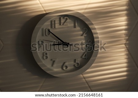 White big analogue plain wall clock on trendy hexagon ceramic tiles background. Very nice striped light from sunset. Near nine o'clock. Time management concept, opening or closing hours