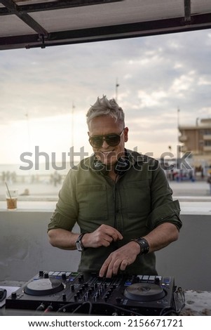 Deejay mixing outdoor with back sun light - Portrait of disc jockey playing disco or deep music for people on beach party at sunset - Backlight with focus on face