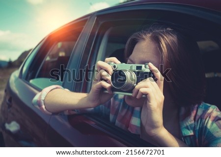 Summer Road Trip. Girl with retro camera taking pictures from the car window. 
