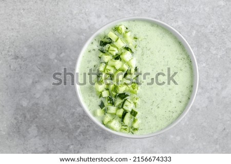 Green fresh cold summer soup decorated with pieces of cucumber and herbs on gray background. top view. Healthy food concept. High quality photo